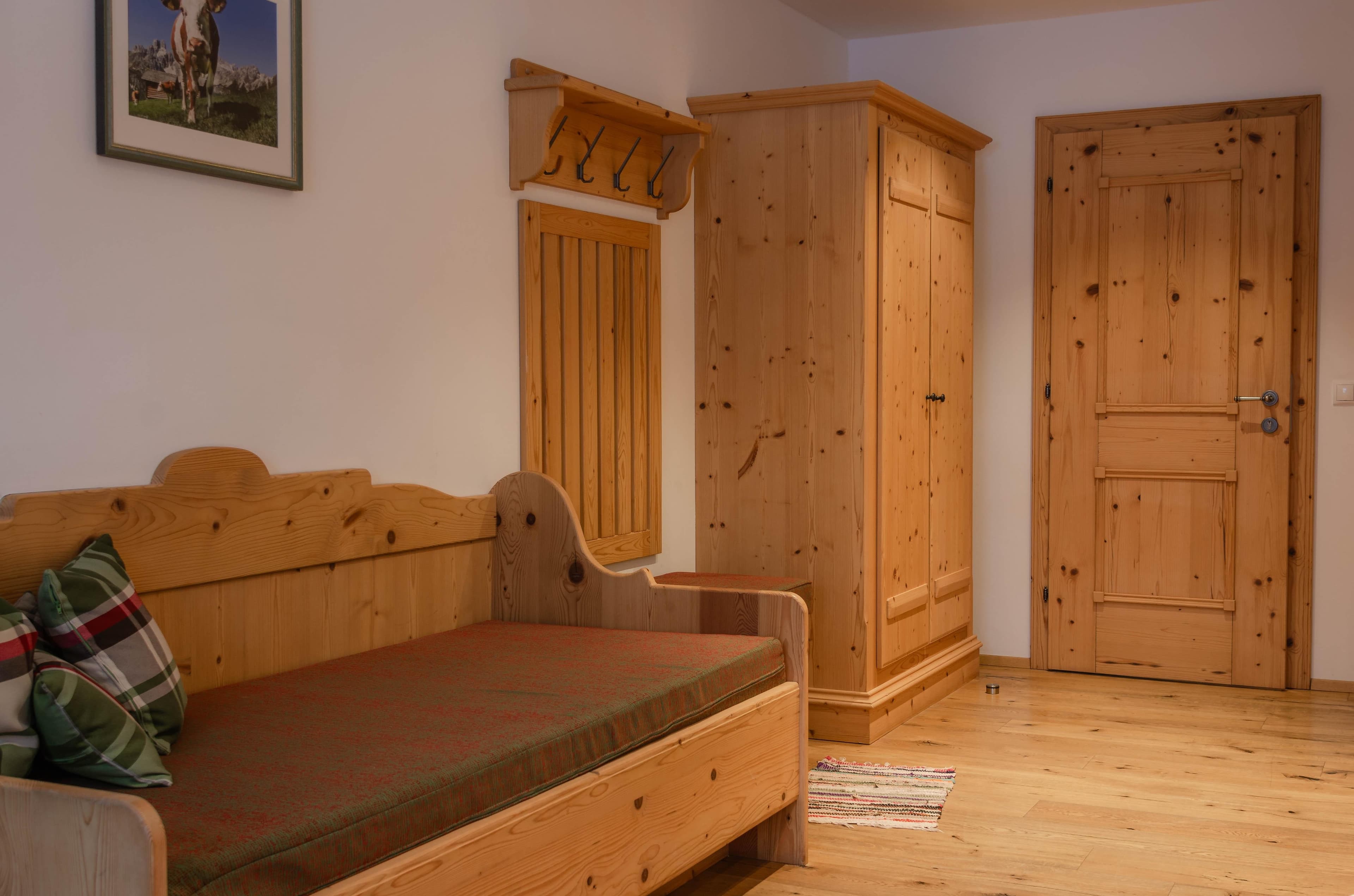 Bauernhof Krahlehen · Dreibettzimmer mit Frühstück - Bright bedroom with a wooden double bed and an adjacent wooden daybed, featuring a large window and a glass door leading to a balcony. Outside, snow-covered mountains and trees are visible, suggesting a winter mountain view. The room is cozy and inviting.